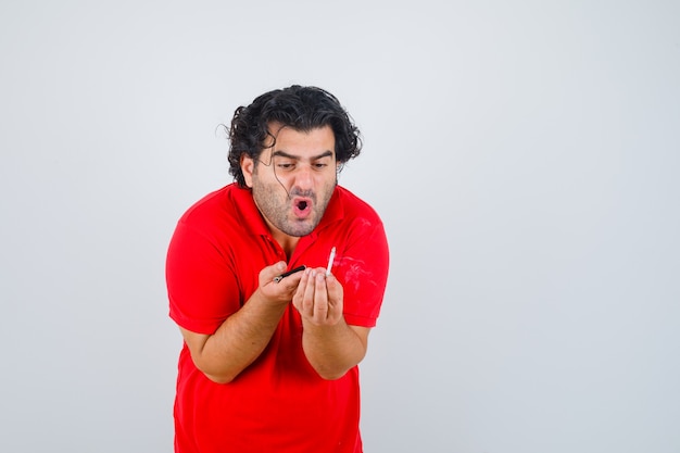 Photo gratuite bel homme tenant la cigarette, en le regardant en t-shirt rouge et regardant concentré, vue de face.