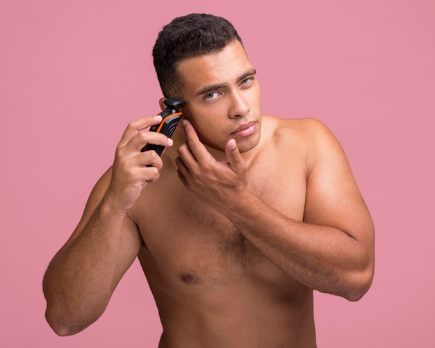 Bel homme torse nu à l'aide d'un rasoir électrique