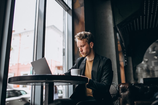 Bel homme travaillant sur un ordinateur dans un café et boire un café