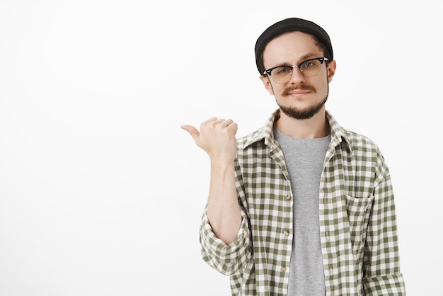 Bel homme urbain sûr de lui avec moustache en bonnet noir souriant indiquant la gauche avec le pouce