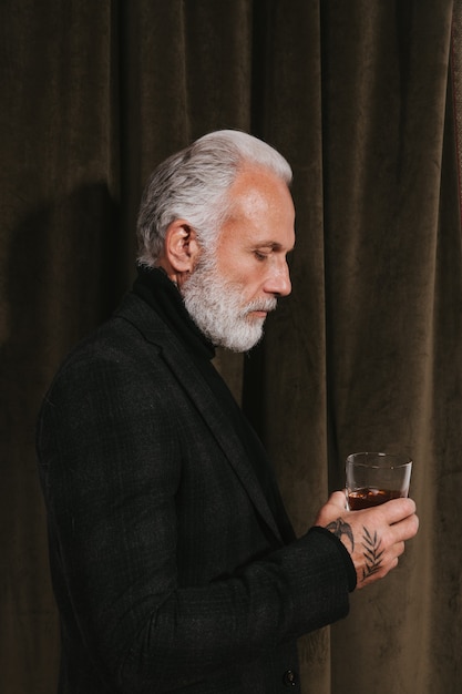 Bel homme en veste noire tient un verre de whisky