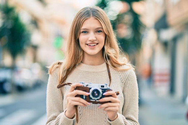 Belle adolescente caucasienne souriante heureuse à l'aide d'un appareil photo vintage à la ville.