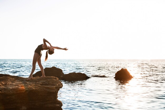 Belle ballerine dansant, posant sur le rocher à la plage, vue sur la mer.