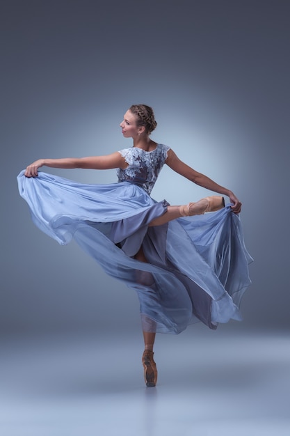 La belle ballerine danse en longue robe bleue sur fond bleu