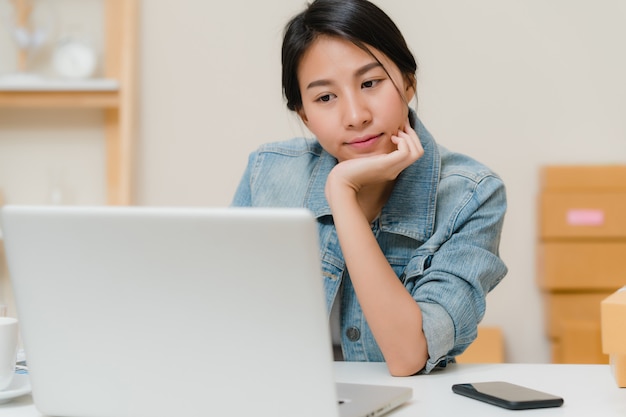 Belle belle asiatique jeune entrepreneur femme d&#39;affaires propriétaire d&#39;une PME en ligne vérifiant le produit en stock et l&#39;enregistrant à l&#39;ordinateur travaillant à la maison.