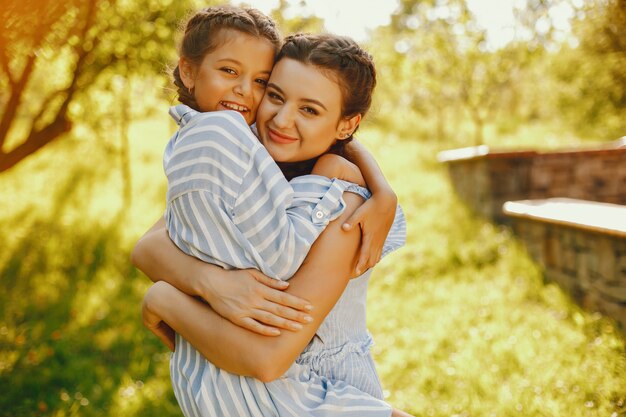 une belle et belle maman aux cheveux longs dans une robe bleue debout dans un parc solaire et en jouant