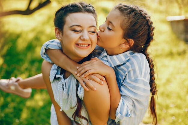 une belle et belle maman aux cheveux longs dans une robe bleue debout dans un parc solaire et en jouant