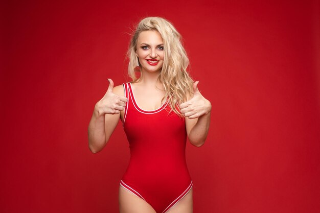 Belle blonde en maillot de bain rouge avec maquillage lumineux et lèvres rouges