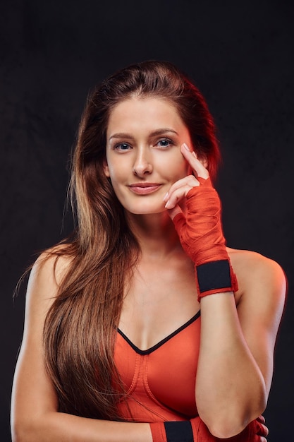 Belle boxeuse brune pensive en soutien-gorge de sport avec les mains bandées. Isolé sur un fond texturé sombre.