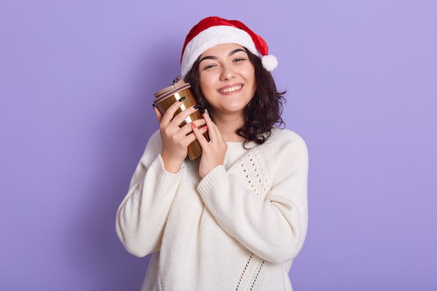 Belle brune femme heureuse en bonnet de Noel et chandail tricoté tenant une tasse thermo