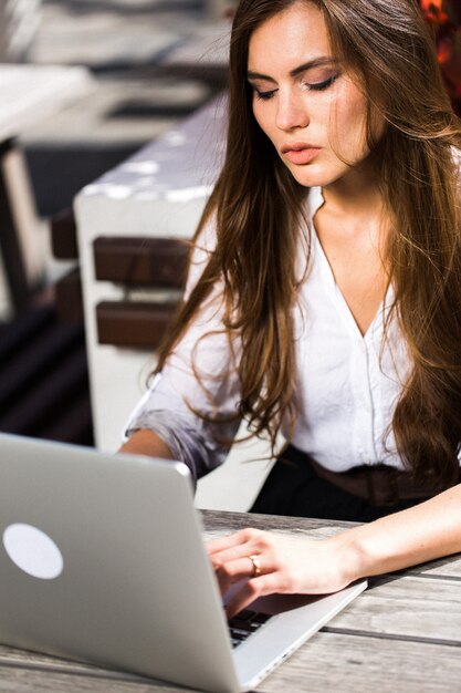 Belle brune travaille avec un ordinateur portable à l&#39;extérieur