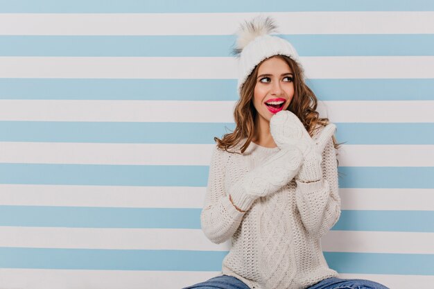 Photo gratuite belle et charmante jeune femme regarde sournoisement vers la gauche et fait une expression surprise sur son visage. portrait sur mur bleu et blanc isolé