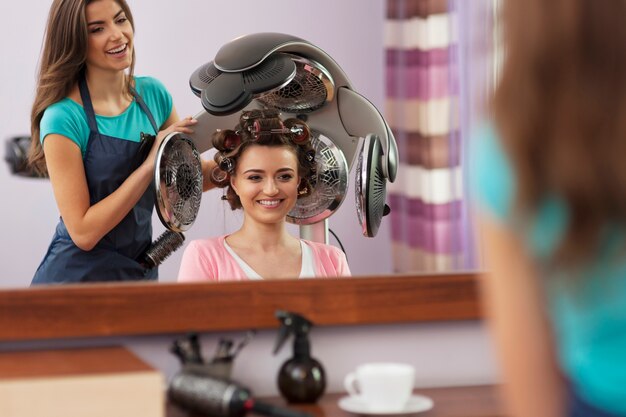 Belle cliente assise sous un sèche-cheveux avec rouleaux