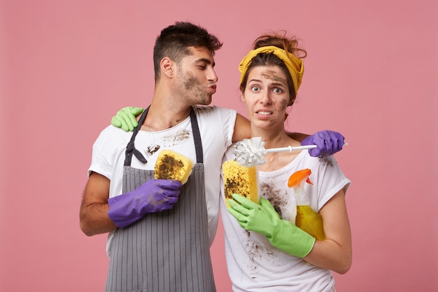 Belle coupe: bel homme embrassant sa femme voulant l'embrasser en l'aidant à nettoyer leur maison