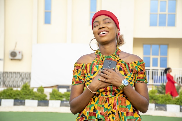 Belle dame africaine tenant son téléphone contre sa poitrine remplie de joie