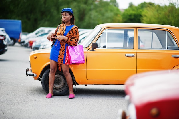 Belle dame afro-américaine avec des sacs à provisions debout près d'une voiture rétro classique orange