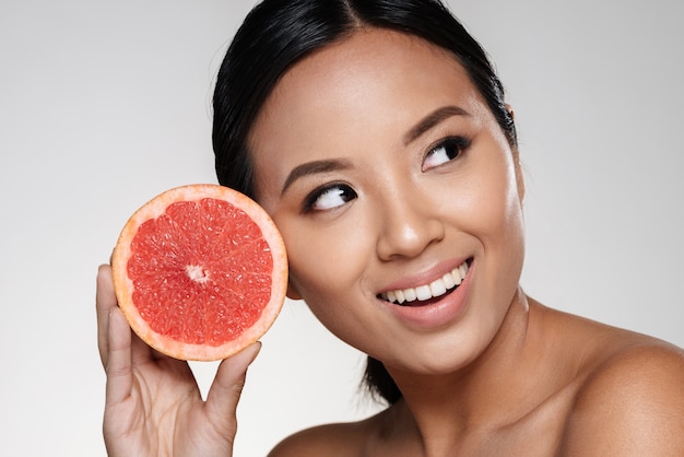 belle dame asiatique regardant de côté et tenant une tranche de pamplemousse près du visage