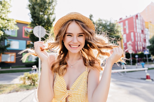 Belle dame bouclée en tenue jaune à la mode appréciant le matin. Photo extérieure d'une fille géniale s'amusant en ville.