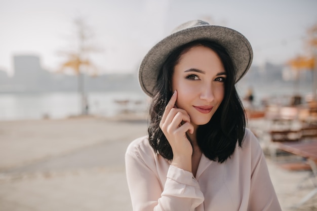 Belle dame brune au chapeau touchant son visage de manière ludique