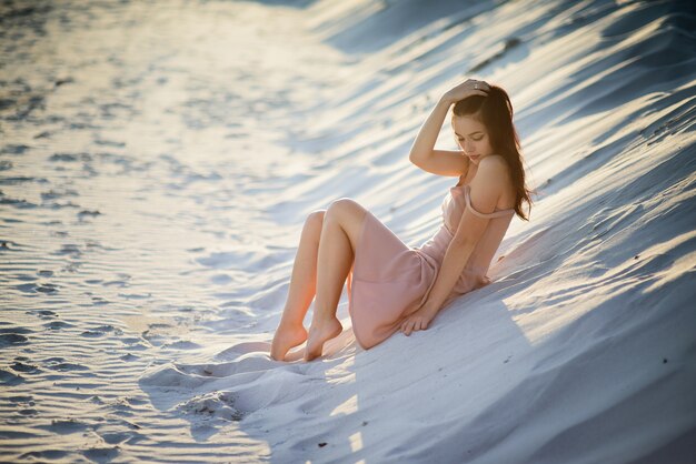 Belle dame brune repose sur le sable blanc dans les rayons du soleil