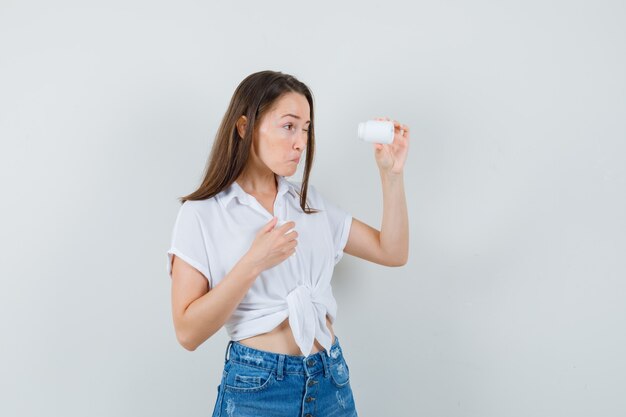 Belle dame en chemisier blanc à l'intérieur de la bouteille de pilules et à la vue de face, focalisée.