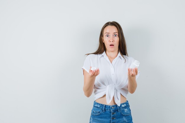 Belle dame montrant une bouteille de pilules en chemisier blanc et l'air inquiet. vue de face. espace pour le texte