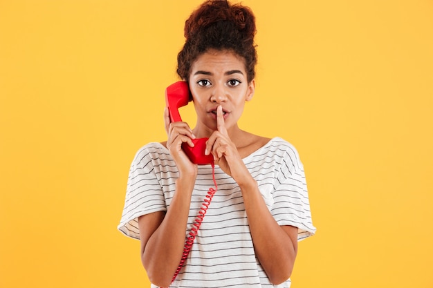 Belle dame montrant le geste de silence tout en parlant sur le combiné rouge