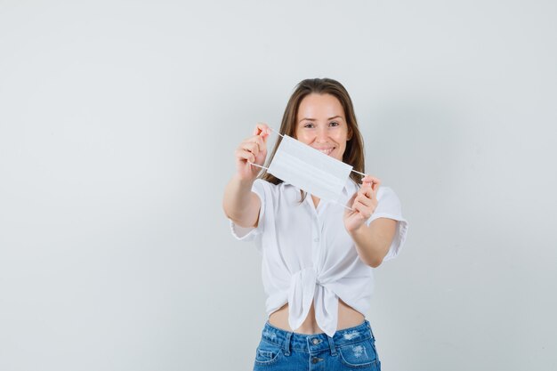 Belle dame montrant un masque facial en chemisier blanc, jeans et à la joyeuse vue de face. espace libre pour votre texte