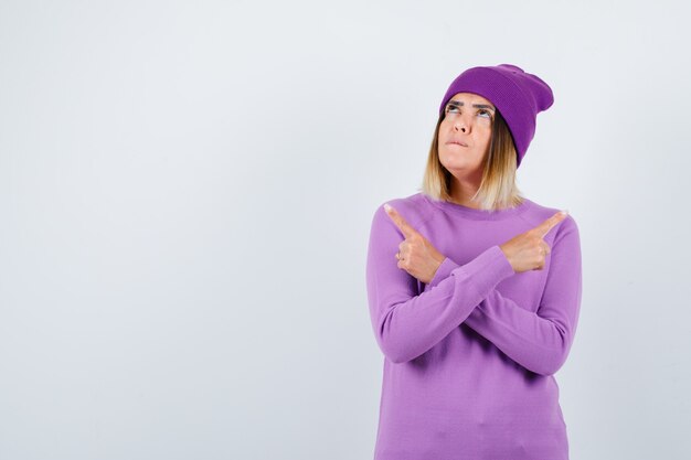 Belle dame pointant vers les côtés gauche et droit en pull, bonnet et semblant confiante. vue de face.