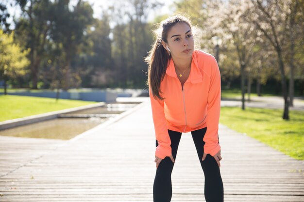 Belle dame sportive se penchant sur les genoux et se détendre dans le parc de la ville