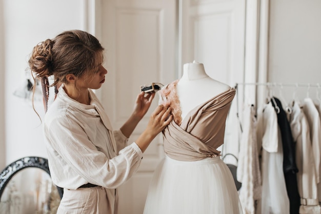 Belle dame en tenue beige crée une nouvelle robe Femme brune en chemise blanche et pantalon concevant une tenue à la mode