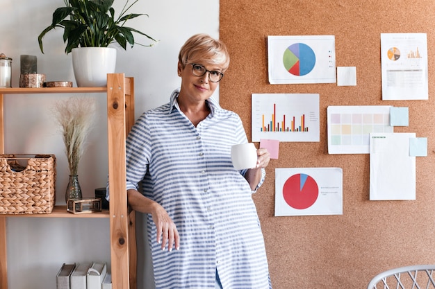 Belle dame en tenue rayée pose avec une tasse de thé au bureau