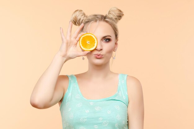 Une belle douce charmante femme lumineuse fraîche avec une coiffure cool tient des tranches d'orange dans sa main