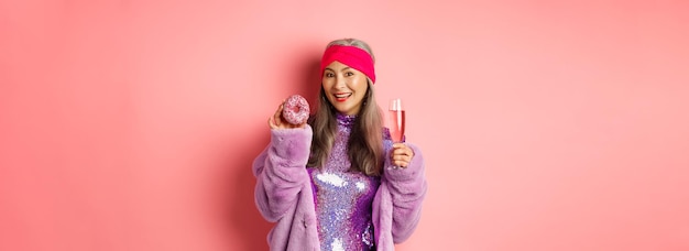 Belle et élégante femme âgée asiatique s'amusant à boire du champagne et à manger un beignet sucré smilin