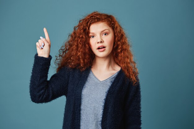 Belle étudiante au gingembre avec des taches de rousseur en t-shirt gris et un cardigan noir pointant à l'envers avec une expression de visage heureuse et détendue. Espace copie ..