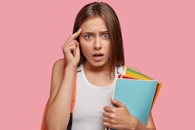 Belle étudiante stressante posant contre le mur rose