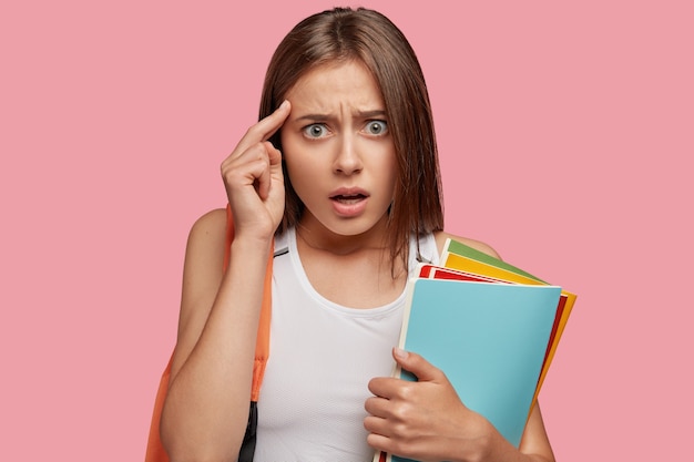 Belle étudiante stressante posant contre le mur rose