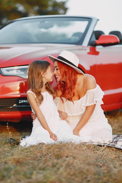 Belle famille dans un parc. Femme en robe blanche et chapeau. Mère avec fille assise sur une couverture.