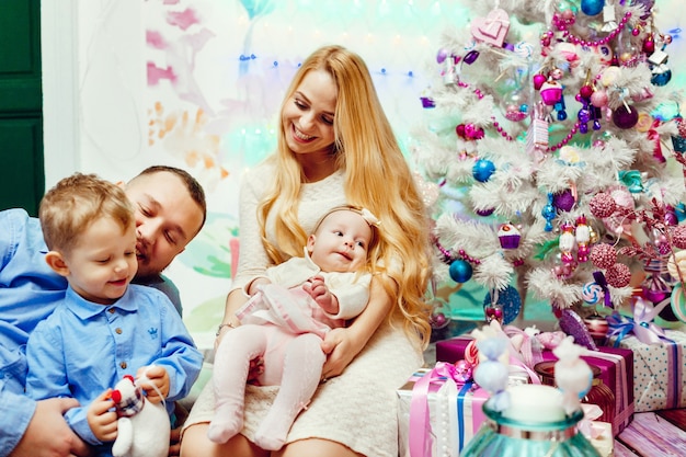 Belle Famille Avec Des Enfants Dans Des Chandails Chauds Pose Devant Un Mur Et Un Arbre De Noël Riche