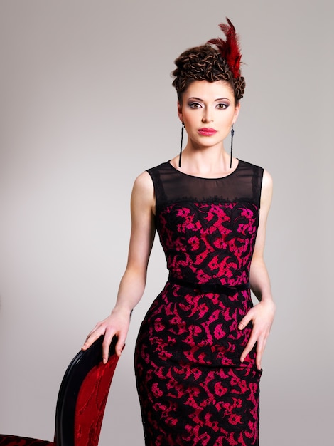 Belle femme adulte avec une coiffure de mode et un fauteuil rouge pose au studio