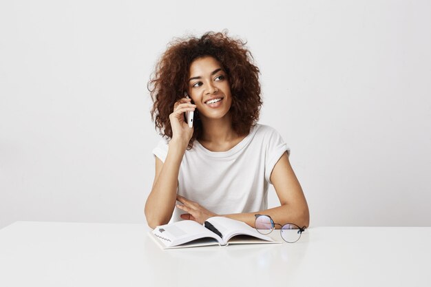 Belle femme d'affaires africaine gaie parlant au téléphone sur le mur blanc.