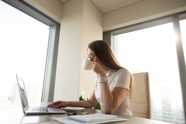 Belle femme d&#39;affaires, boire du café tout en travaillant sur un ordinateur portable au lieu de travail