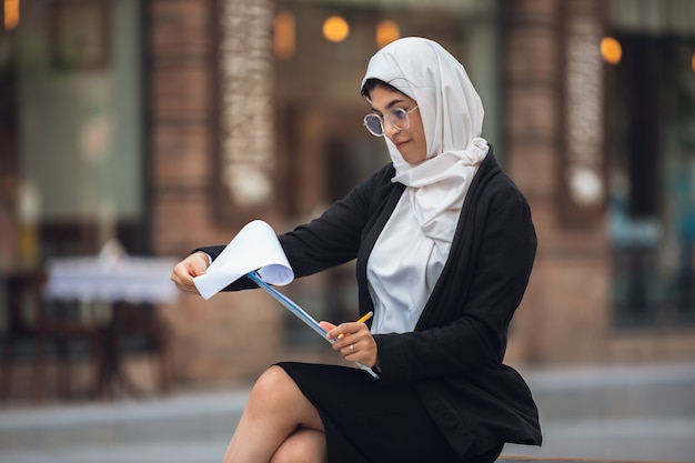 Belle femme d'affaires musulmane réussie lisant un document dans la rue