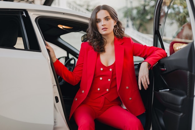 Belle femme d'affaires riche sexy en costume rouge posant dans une voiture blanche