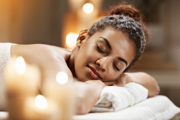 Belle femme africaine au repos relaxante dans une station thermale avec les yeux fermés.