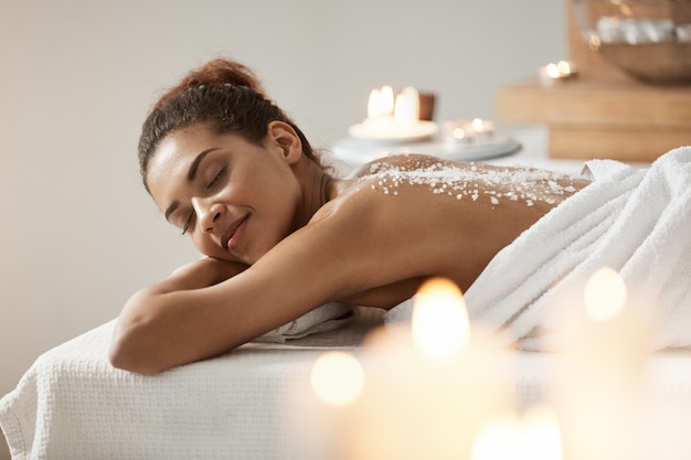 Photo gratuite belle femme africaine au repos relaxante avec du sel de mer sur le dos dans le salon spa.