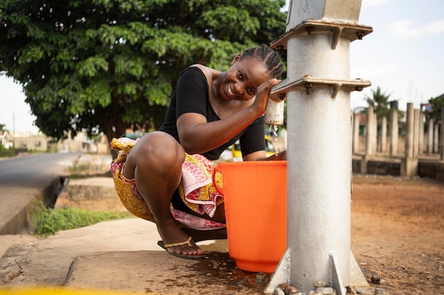 Photo gratuite belle femme africaine mettant de l'eau dans un seau