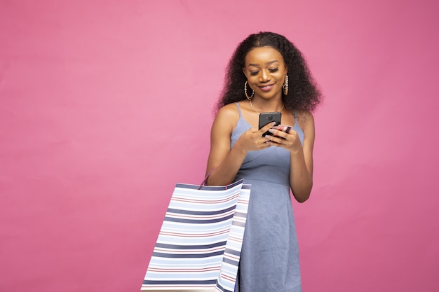 Belle femme africaine postant dans les médias sociaux à l'aide de son smartphone à propos de sa virée shopping