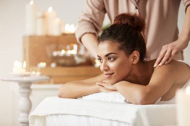 Belle femme africaine souriante appréciant le massage dans la station thermale.