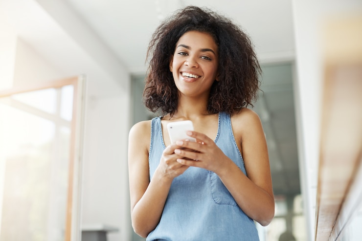 Photo gratuit belle femme africaine souriante tenant le téléphone assis dans le café.